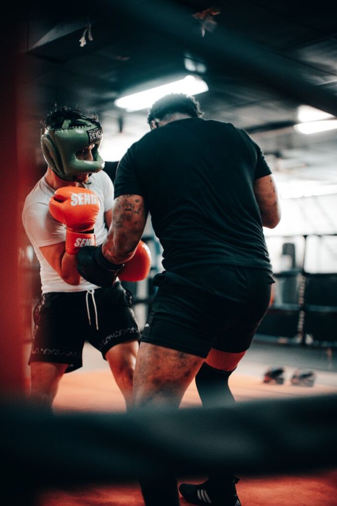 Two men engaged in an intense boxing sparring session with protective gear in a gym setting.